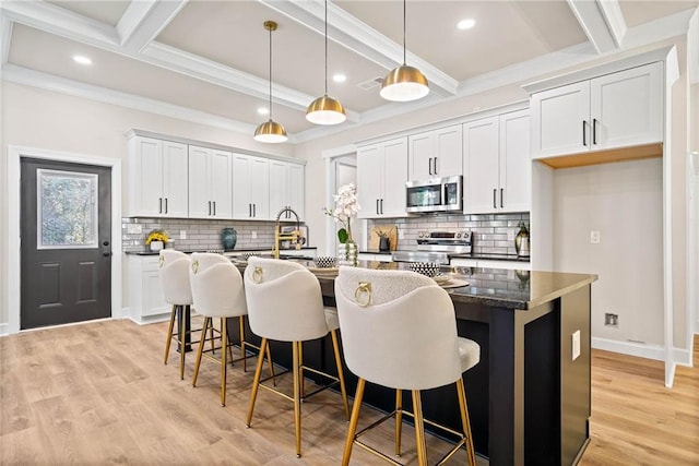 kitchen featuring beam ceiling, an island with sink, light wood finished floors, and stainless steel appliances
