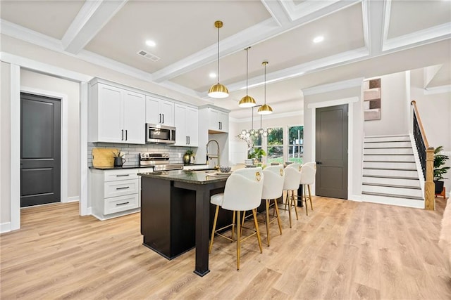 kitchen featuring dark countertops, beamed ceiling, a breakfast bar, stainless steel appliances, and a kitchen island with sink