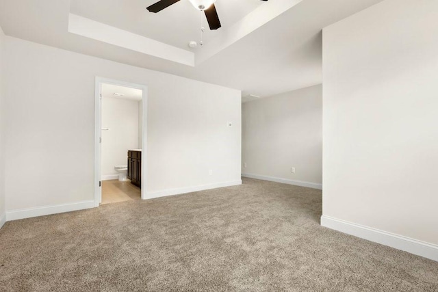unfurnished room featuring light colored carpet, a ceiling fan, a raised ceiling, and baseboards