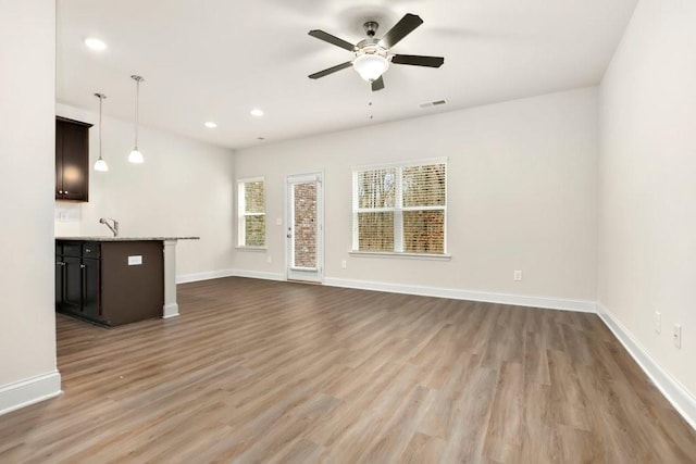 unfurnished living room with baseboards, a ceiling fan, wood finished floors, and visible vents