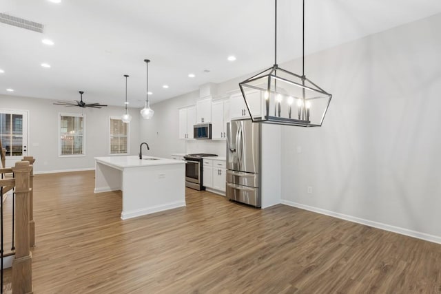 kitchen with appliances with stainless steel finishes, sink, a center island with sink, white cabinets, and hanging light fixtures