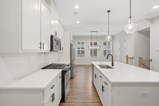 kitchen with stainless steel appliances, white cabinetry, hanging light fixtures, and a center island with sink