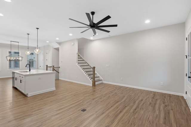 kitchen featuring ceiling fan, hanging light fixtures, light hardwood / wood-style floors, a kitchen island with sink, and white cabinets