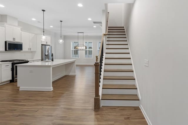 kitchen with white cabinetry, hanging light fixtures, stainless steel appliances, dark hardwood / wood-style flooring, and a kitchen island with sink