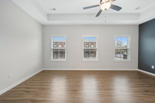 unfurnished room featuring ceiling fan, dark wood-type flooring, and a tray ceiling