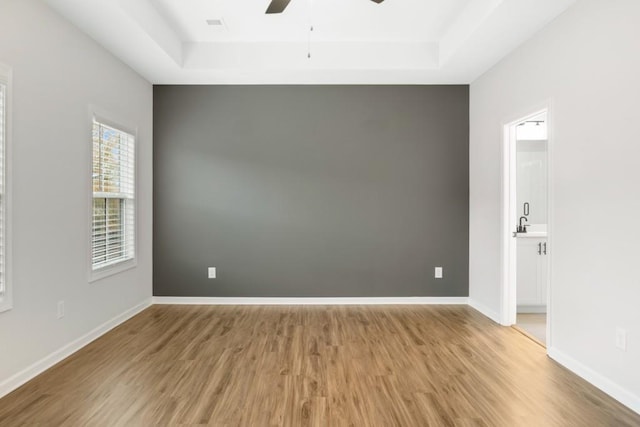 empty room with a tray ceiling, ceiling fan, and light hardwood / wood-style floors