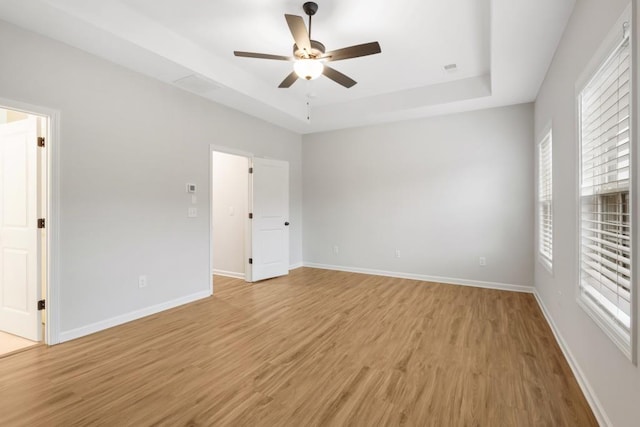 unfurnished room featuring ceiling fan, a raised ceiling, and light wood-type flooring