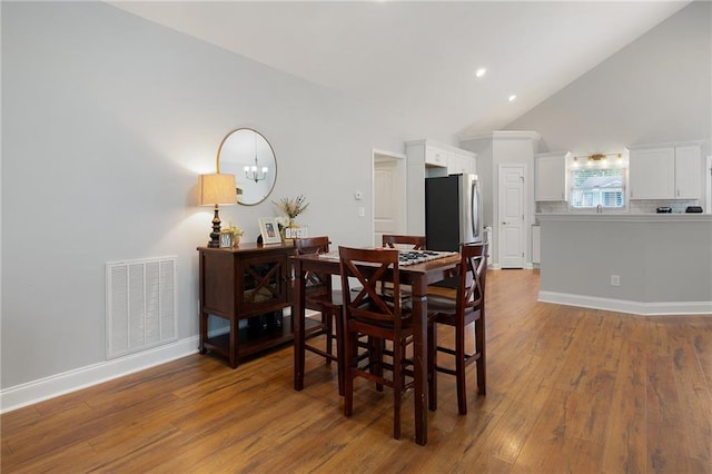 dining space featuring high vaulted ceiling, wood-type flooring, visible vents, and baseboards