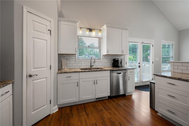 kitchen with stone countertops, white cabinets, vaulted ceiling, a sink, and dishwasher