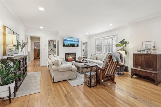 living room with built in shelves, ornamental molding, a fireplace, and light wood-type flooring