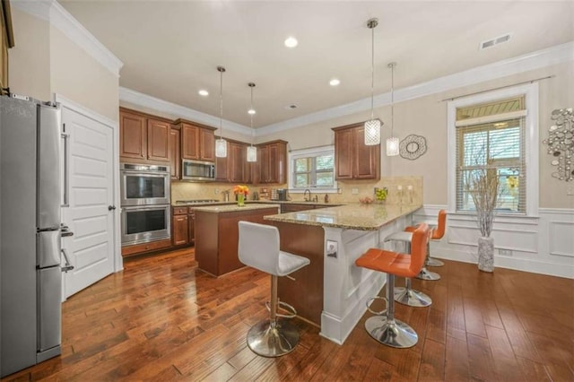 kitchen with a breakfast bar area, light stone counters, decorative light fixtures, appliances with stainless steel finishes, and kitchen peninsula