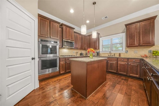 kitchen featuring decorative light fixtures, appliances with stainless steel finishes, a kitchen island, light stone countertops, and decorative backsplash