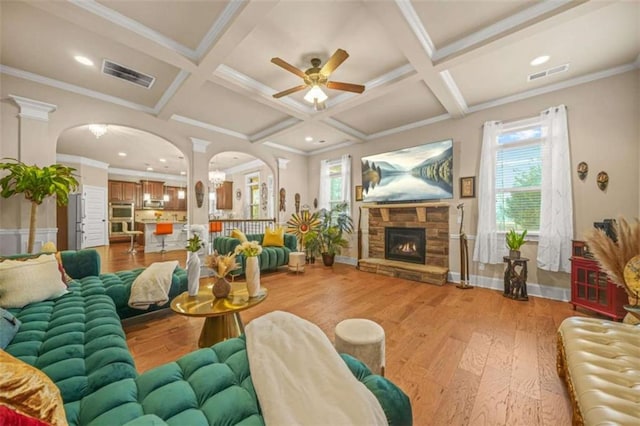 living room featuring coffered ceiling, a stone fireplace, light hardwood / wood-style floors, and beamed ceiling