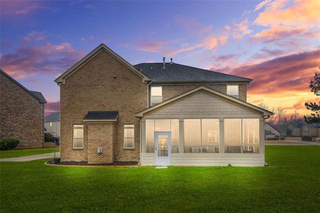 back house at dusk featuring a lawn and a sunroom