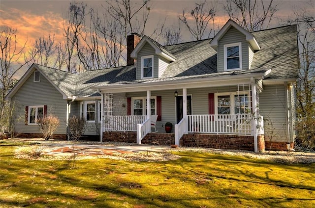 cape cod house with covered porch, a shingled roof, a chimney, and a front lawn