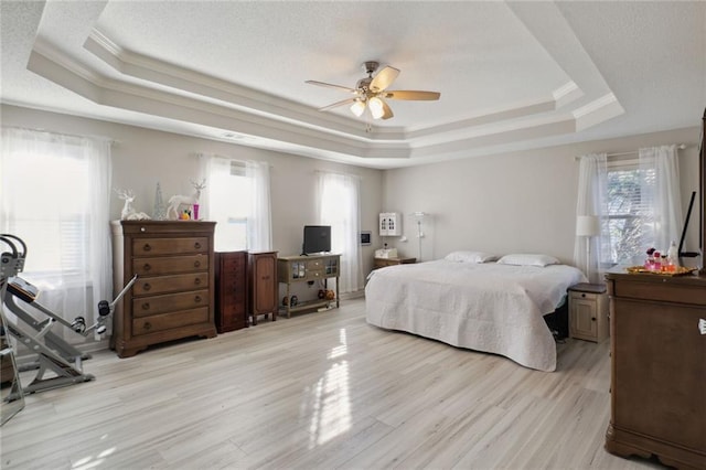 bedroom with light wood-type flooring, ornamental molding, a tray ceiling, and ceiling fan