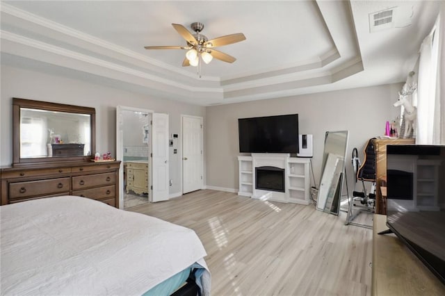 bedroom with ceiling fan, ensuite bathroom, light wood-type flooring, and a tray ceiling