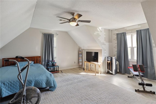 bedroom featuring light wood-type flooring, lofted ceiling, ceiling fan, and a textured ceiling