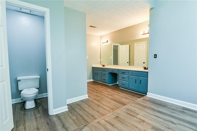 bathroom featuring baseboards, toilet, wood finished floors, and double vanity