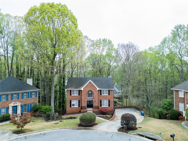 view of front of house with a chimney, brick siding, driveway, and a front lawn