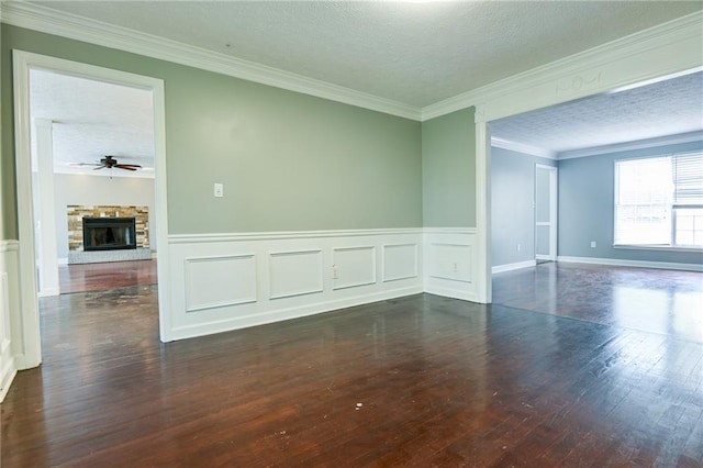 empty room with a stone fireplace, a textured ceiling, crown molding, and wood finished floors
