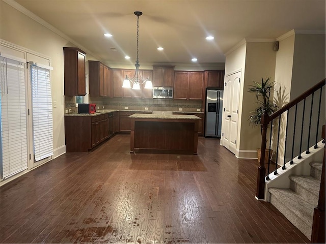 kitchen featuring crown molding, dark wood-type flooring, appliances with stainless steel finishes, a center island, and decorative light fixtures