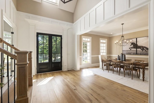 entrance foyer with french doors, a high ceiling, a notable chandelier, light wood-type flooring, and crown molding