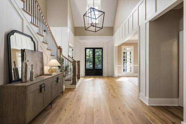 entrance foyer with french doors, an inviting chandelier, light wood-type flooring, and high vaulted ceiling