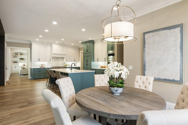 dining room with ornamental molding, sink, and light hardwood / wood-style floors