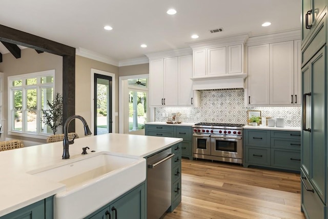 kitchen with light hardwood / wood-style floors, beam ceiling, sink, high end appliances, and white cabinetry