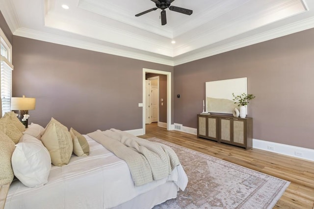 bedroom featuring crown molding, a tray ceiling, hardwood / wood-style flooring, and ceiling fan