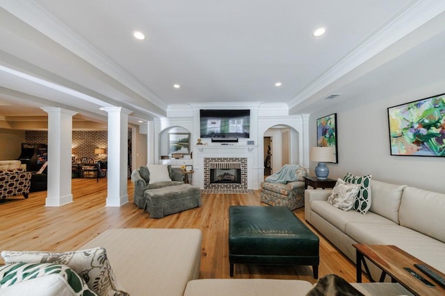 living room featuring a brick fireplace, ornamental molding, decorative columns, and wood-type flooring