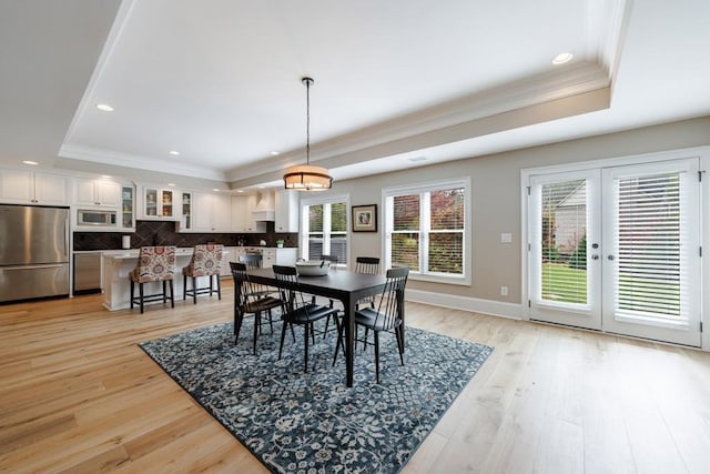 dining room featuring a raised ceiling, french doors, light hardwood / wood-style flooring, and ornamental molding