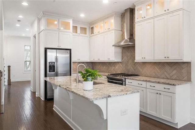 kitchen featuring wall chimney range hood, stainless steel appliances, an island with sink, and white cabinets