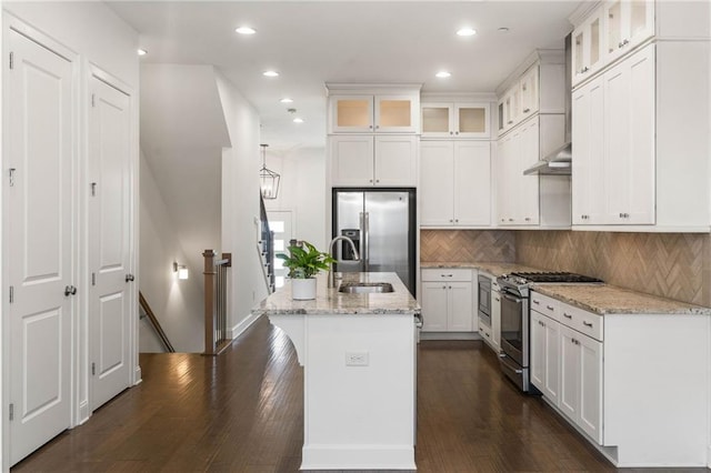 kitchen with stainless steel appliances, light stone countertops, a center island with sink, and white cabinets