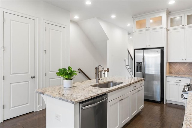 kitchen featuring sink, white cabinetry, stainless steel appliances, light stone countertops, and a center island with sink