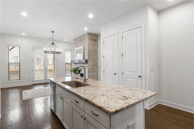 kitchen with sink, hanging light fixtures, dishwasher, light stone countertops, and a kitchen island with sink