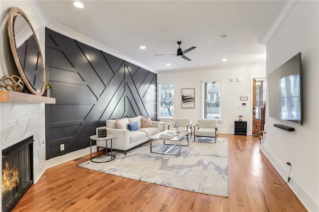 living room with ceiling fan, light hardwood / wood-style floors, ornamental molding, and a tile fireplace