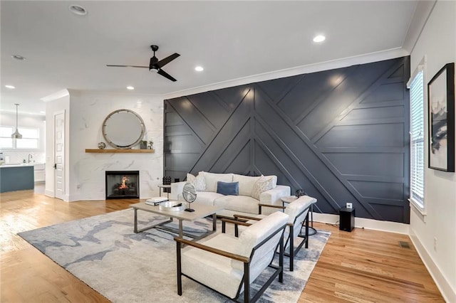 living room featuring a fireplace, light hardwood / wood-style flooring, ceiling fan, and crown molding