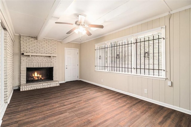 unfurnished living room with dark wood finished floors, a ceiling fan, ornamental molding, a brick fireplace, and beam ceiling