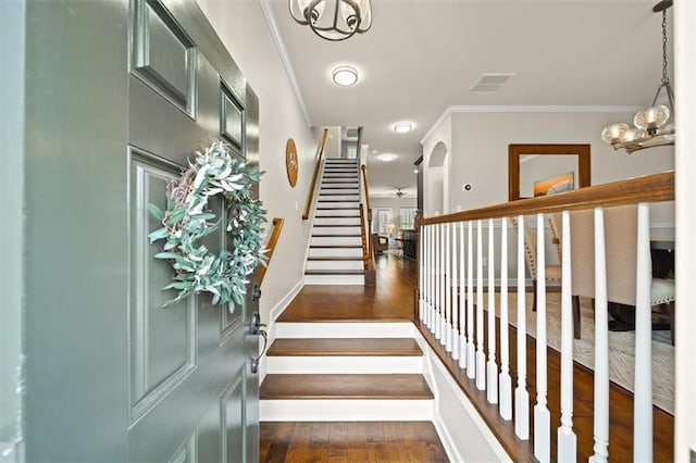 stairs featuring wood-type flooring, a notable chandelier, and crown molding