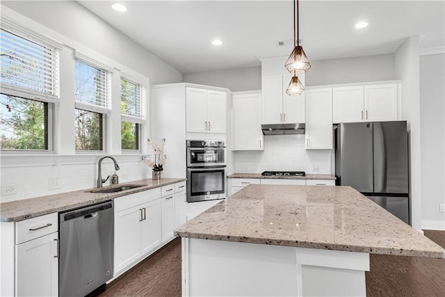 kitchen with under cabinet range hood, stainless steel appliances, a kitchen island, white cabinets, and decorative light fixtures