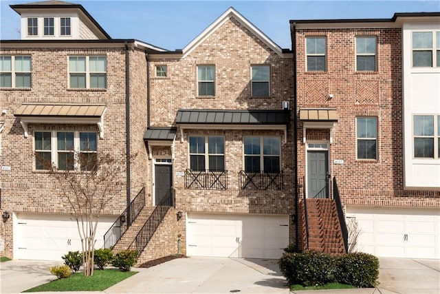 townhome / multi-family property featuring driveway, brick siding, a standing seam roof, and an attached garage