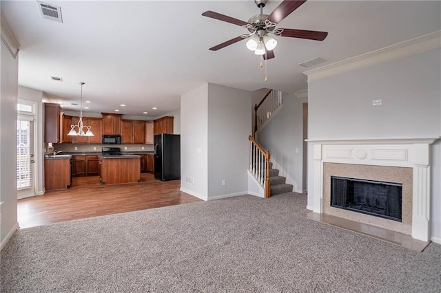 kitchen featuring brown cabinetry, visible vents, black appliances, light carpet, and open floor plan