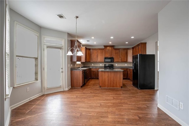 kitchen with wood finished floors, visible vents, black appliances, dark countertops, and tasteful backsplash