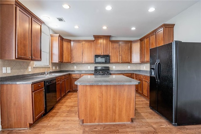 kitchen featuring visible vents, a kitchen island, a sink, black appliances, and light wood-style floors