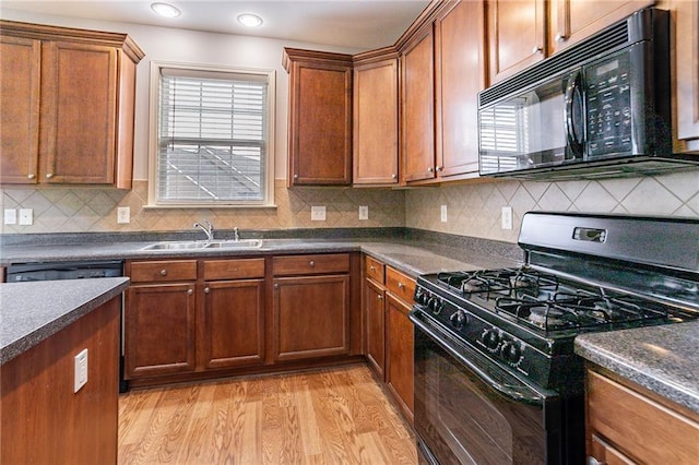 kitchen with a wealth of natural light, black appliances, a sink, dark countertops, and light wood-style floors