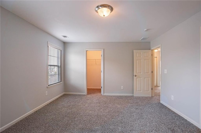 unfurnished bedroom featuring a spacious closet, baseboards, visible vents, and carpet floors