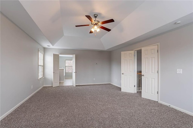 carpeted empty room with visible vents, baseboards, a tray ceiling, and ceiling fan