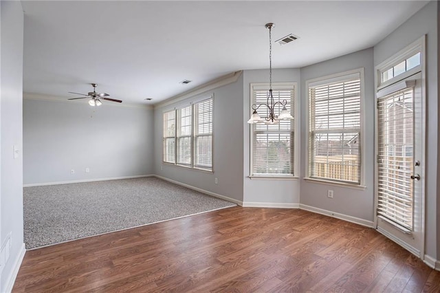 unfurnished dining area with visible vents, ceiling fan with notable chandelier, wood finished floors, crown molding, and baseboards